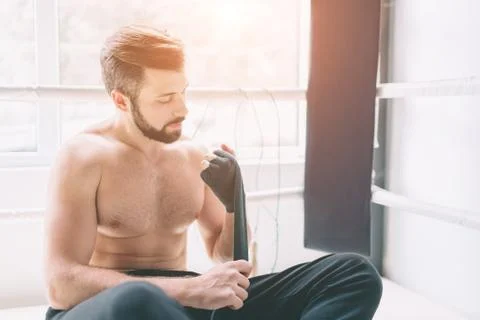 Handsome bearded boxer with bare torso wrapping his hands, ready to fight at the Stock Photos