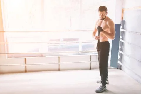 Handsome bearded boxer with bare torso wrapping his hands, ready to fight at the Stockfoto's