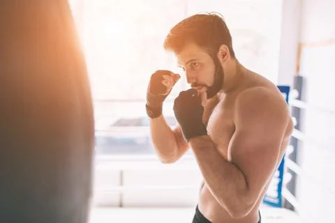 Handsome bearded boxer with bare torso is practicing punches at the fight club Stock Photos