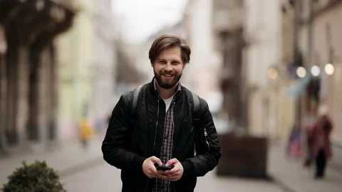 Handsome bearded Caucasian man Using a Smartphone on a Street. He Smiles and Stock Footage 152477760