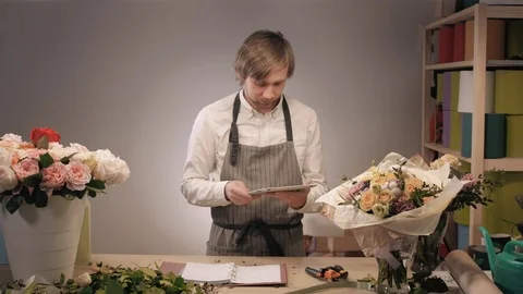 Handsome bearded florist with tablet computer at workplace taking order by phone Stock Footage 71978401