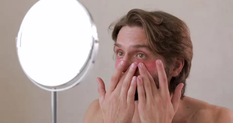 Handsome bearded guy with bare shoulder using cosmetic patches under eyes while Stock Footage 142527745