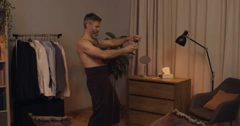 Handsome bearded guy in bath towel pouring elite alcohol into glass and drinking 動画素材 136481347