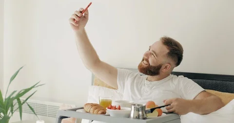 Handsome bearded guy doing selfie while having breakfast in morning. Man in 30s Stock Footage 129389165