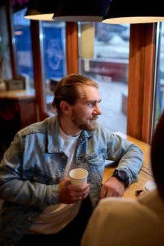 Handsome bearded guy drinking coffee in cafe, smiling, looking at side Foto stock
