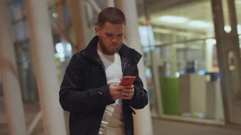 Handsome bearded guy in jacket browsing intenet content on smartphone while Stock Footage 117429762
