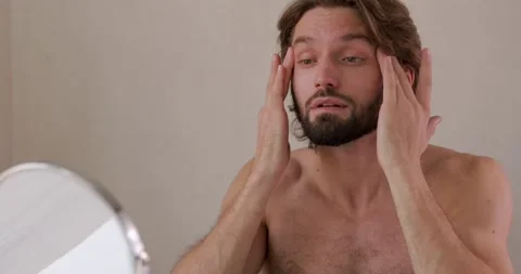 Handsome bearded man applying mask on face for reduce wrinkles while looking at Stock Footage 142528778