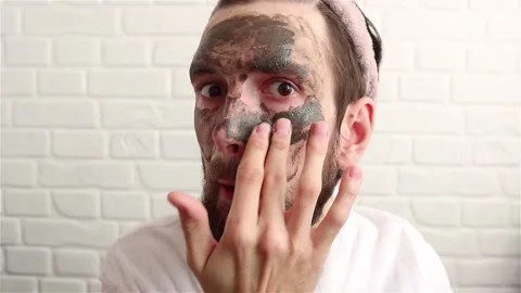 Handsome bearded man in bathrobe applying dark cosmetic facial mask close up Stock Footage 150344623