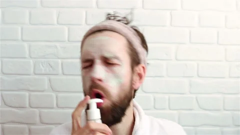 Handsome bearded man in bathrobe singing with pump bottle from cream having fun Stock-Footage 153958193