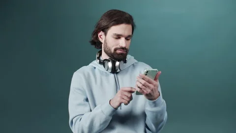 A handsome bearded man in a blue sweater is using a phone and searching through Stock Footage 170914441