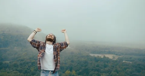 Handsome bearded man dances on the top of a mountain like a winner Stock Footage 94924265