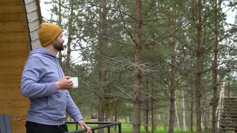 Handsome bearded man drinking hot tea in front of a modern wooden house Stock Footage 240955036