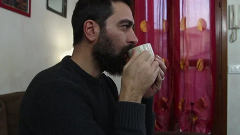 Handsome bearded man drinks a cup of hot tea sitting on the sofa Stock Footage 142817660