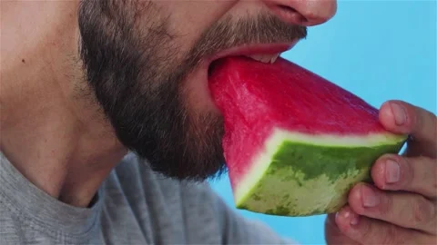 Handsome bearded man eats juicy watermelon close up on blue background Vidéo 122801559