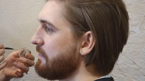 Handsome bearded man getting makeup by stylist at the beauty studio.  Video stock 74615601