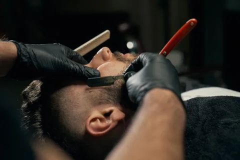 Handsome bearded man is getting shaved by hairdresser Stock Photos