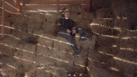 Handsome bearded man in glasses with blond hair sitting on the hay with a straw Stock Footage 104124243