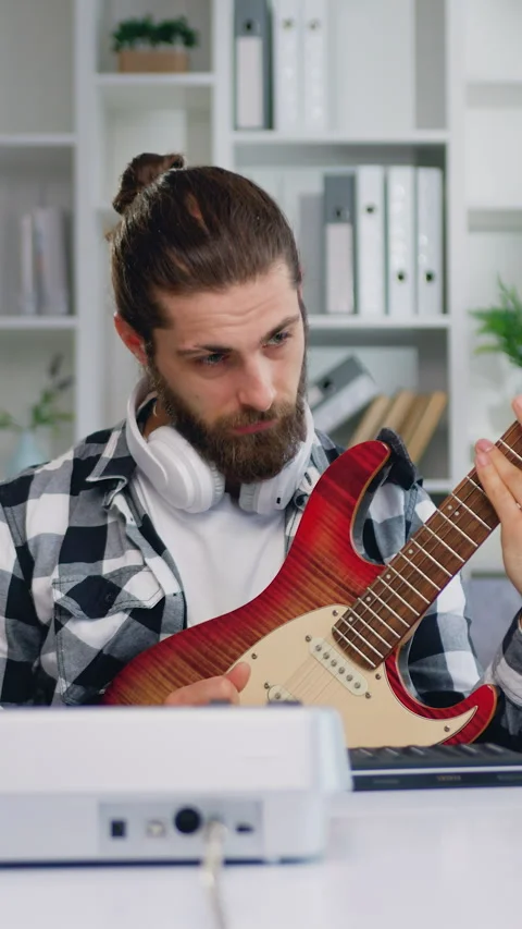 Handsome bearded man having online electric guitar class sitting at the desk in  Stock Footage 334433311