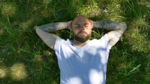 Handsome bearded man lying on grass and stretch himeself in summer slow motion Stock-Footage 96296305