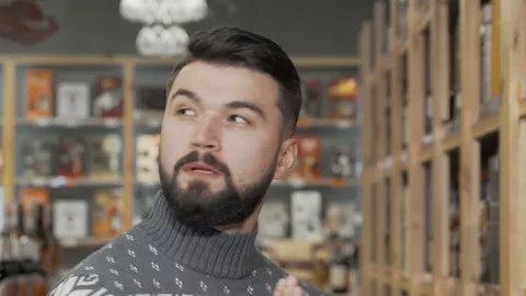 Handsome bearded man thoughtfully selecting wine at a stylish supermarket Stock Footage 311985445