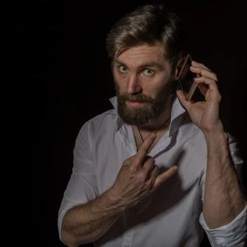 Handsome bearded man using his phone with smile on a dark background Photos