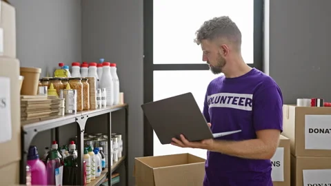 Handsome bearded man using laptop in warehouse with donations and supplies .. Video stock 262203523