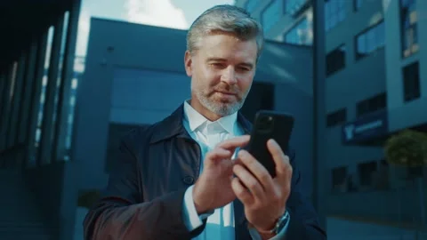 Handsome bearded man using mobile phone near corporate office. Professional Stock Footage 166523686