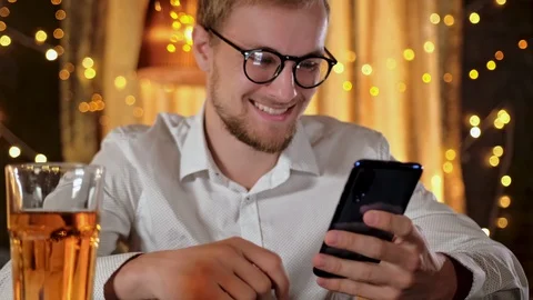Handsome bearded man using a smartphone and smiling while drinking beer in pub Stock Footage 122013567