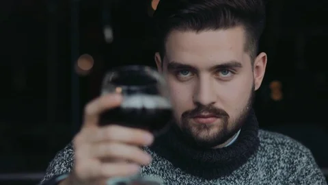 Handsome bearded man in a warm sweater toasts the glass of wine,and smiles Stock Footage 74793239