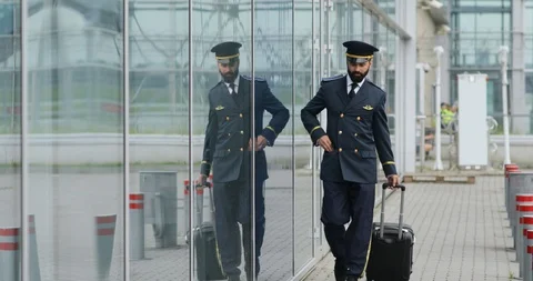 Handsome bearded pilot in a uniform walks by the airport terminal, receives a Stock Footage 92815524