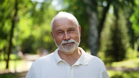 Handsome bearded senior man with gray-hair standing posing in sunshine at summer Stock Footage 287347472