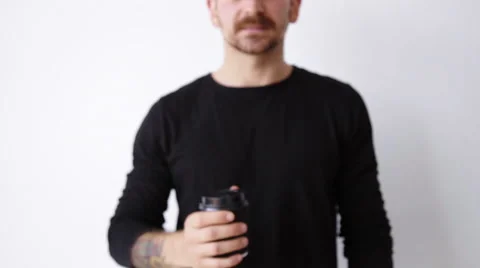 Handsome bearded unfocused guy shows paper cup on camera Stock Footage 64484784