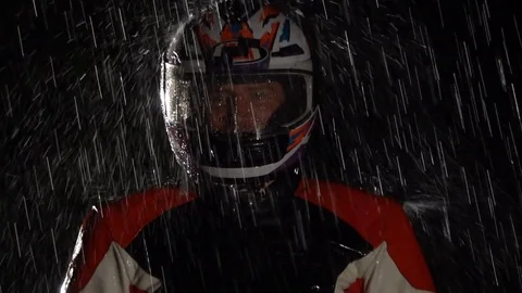 Handsome biker in helmet standing in the rain, looking in the camera. Close up. Stock Footage 80388047
