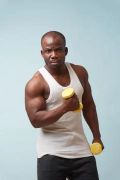 Handsome black man doing biceps curls with light dumbbells. pale blue backgro Stock Photos