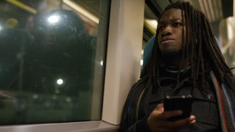 Handsome black man with dreadlocks checking his phone on a train at night Stock Footage 100650746