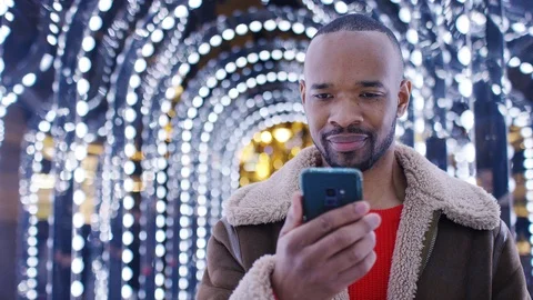 Handsome black man walks through a tunnel of light on his phone, in slow motion Stock Footage 100326845