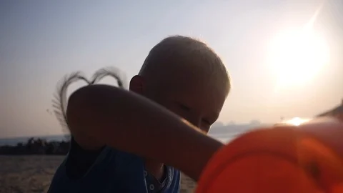 A handsome blond boy playing with sand and a bucket by the sea at sunset. slow Stock Footage 87448857