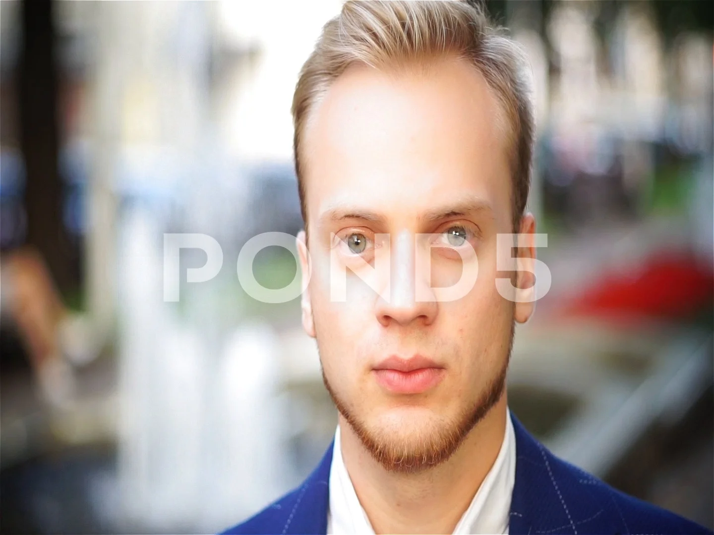 Handsome blond man in a park. A guy with blue eyes in a jacket.