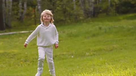 Handsome blonde boy running in the light of the sun on a green lawn Video stock 45430041