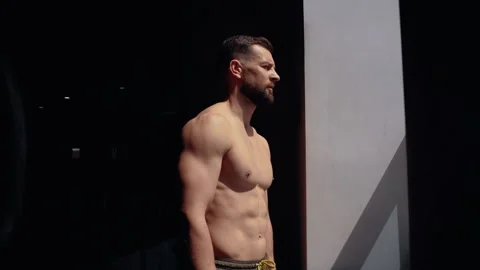 The handsome bodybuilder appears from the shadows, and the light accentuates his Video stock 156480924