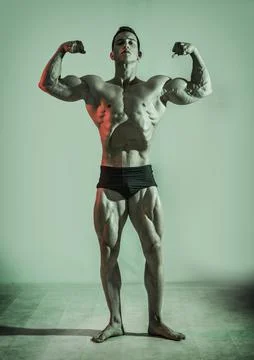 Handsome bodybuilder doing classic double biceps pose, looking away, on dark Stock Photos