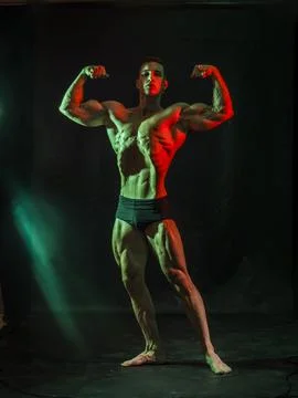 Handsome bodybuilder doing classic double biceps pose, looking away, on dark Stock Photos