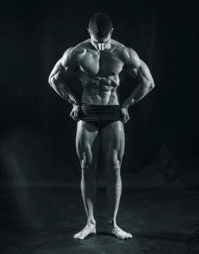Handsome bodybuilder doing classic double biceps pose, looking away, on dark Stock Photos