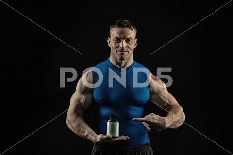 Handsome bodybuilder man with muscular body holds pill jar, steroids Stock Photos