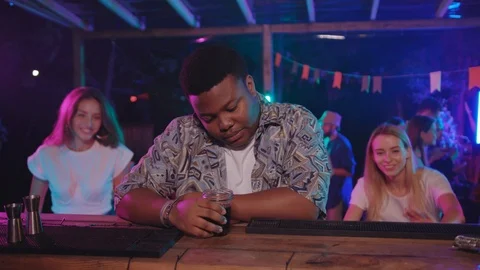 Handsome bored african boy drinking cocktail at bar with two appealing girls Vidéo 115364079