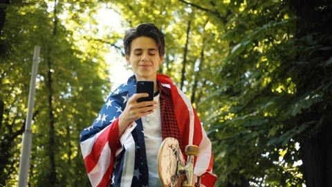 Handsome boy with American flag using a mobile phone smile keeps skate guy Stock Footage 92048715