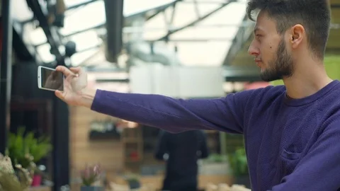 Handsome boy doing selfies on smartphone in the cafe and checking them Video stock 70698189