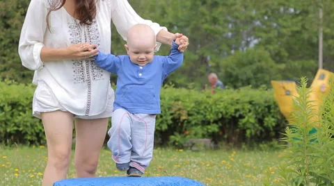 Handsome Boy jumping on a rock in a park with his mother. Baby less than a year Stock Footage 65373254