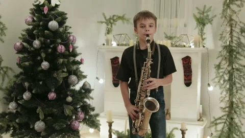 A handsome boy plays the saxophone in the background of the Christmas tree Stock Footage 112335404