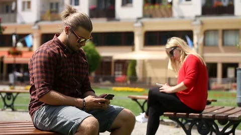 Handsome boy sitting on the bench in the city and texting on smartphone Stock Footage 77473192